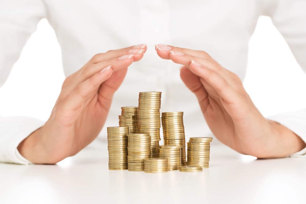 Close-up of female hands protecting a stack of gleaming golden coins symbolizing savings security and financial protection.