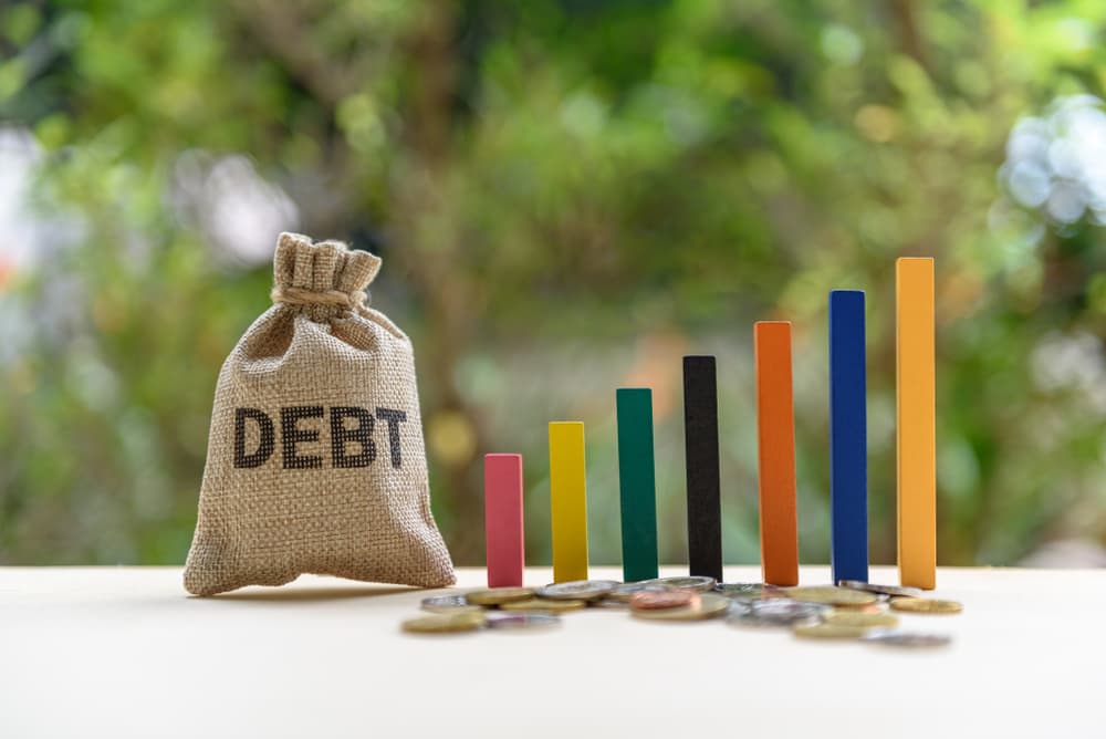 Concept of government or national debt: Colorful wood bar graph, coin, and a debt bag on a table, illustrating the fiscal deficit and accumulated debt due to spending exceeding tax revenue.